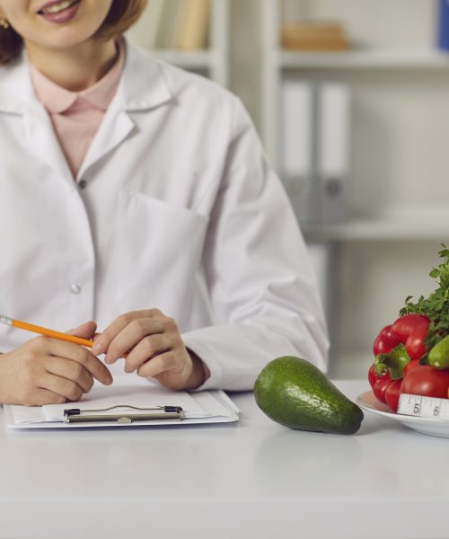 Dietitian sitting at table with fresh fruit, vegetables and individual diet plan